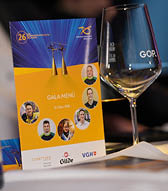 Zwei goldfarbene Skulpturen von Menschen mit B gen stehen vor einem blauen und gelben Hintergrund mit dem Logo und Text des Behinderten-Sportverbands Niedersachsen, daneben ist ein Glas mit unscharfen Aufdrucken zu sehen. Beschreibung von KI generiert